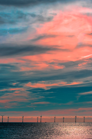 Spiritual awakening. Offshore wind farm cloudscape. Turbines under a pink ethereal sunset sky. Real image lightly simplified creating a beautiful futuristic alien skyscape.の写真素材