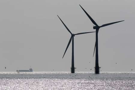 Clean energy. Offshore wind farm turbine silhouette. Naturally monochrome image with supply ship passing on the background horizon. Sustainable renewable resource power production and development.の写真素材