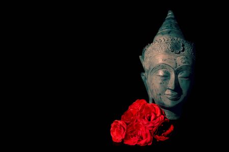 Peace and love. Traditional meditating Buddha head with red roses isolated on black background copyspace. Beautiful peaceful image. Calm Buddhist mindfulness. Zen Buddhism. Spiritual enlightenment.の写真素材