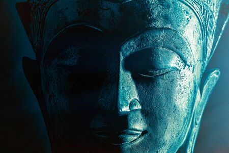 Spiriitual enlightenment. Enlightened buddha face statue close-up. Bold graphic image with atmosperic blue tone light and star highlight. Religious lifestyle awakening via meditation. Serene power.の写真素材