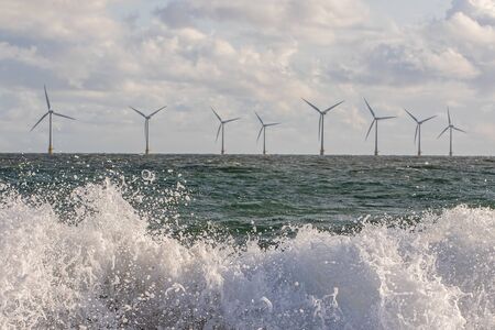 Wind and wave energy. Breaking waves with offshore windfarm turbines background. Sustainable...