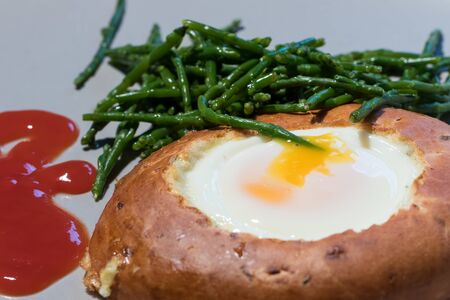 Healthy cooked breakfast meal. Egg in bagel hole with samphire with tomato ketchup. Unusual combination for healthy eating. Close up food presentation.の写真素材