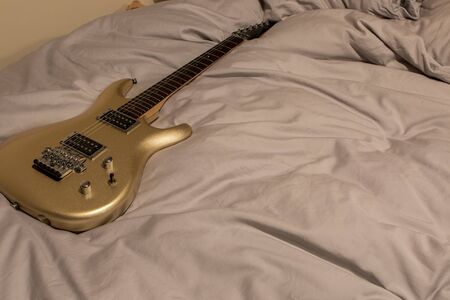 Gold electric guitar lying on a bed. Sexy man toy. Quality musical instrument on a grey duvet. Midlife crisis hobby for the single man.の写真素材