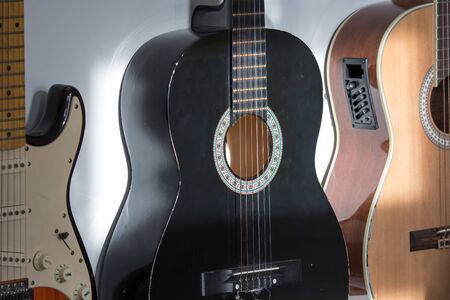 Acoustic and electric guitars hanging on a music room wall. Assorted guitars including a black classical nylon string guitar.の写真素材