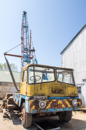 Vintage rusty crane vehicle. Old industrial truck with mounted crane. Retro transport image of scrapyard yellow and blue lorry mounted with lifting gear boom. Farm equipmentの写真素材