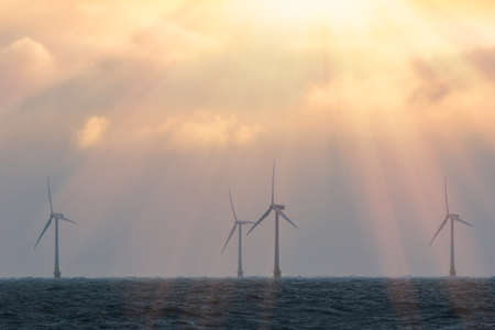 Wind turbines saving the planet. Beautiful spiritual orange pink pastel sky by offshore wind farm at sea. Tackling climate change. Sustainable resource renewable energy from wind solar and wave powerの写真素材