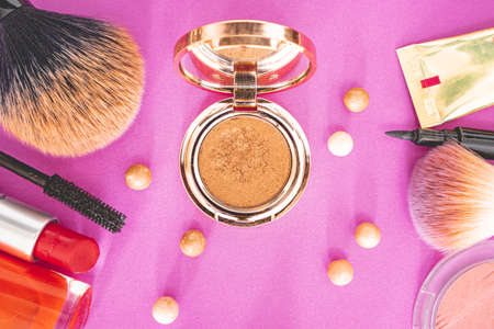 Flat lay of make up and beauty products on a pink background.