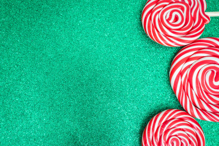 Three Christmas lollypops on a green and glitter backdrop. Wallpaper for Christmas with copy space for text.の写真素材