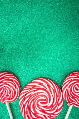 Three Christmas lollypops on a green and glitter backdrop. Wallpaper for Christmas with copy space for text.の写真素材