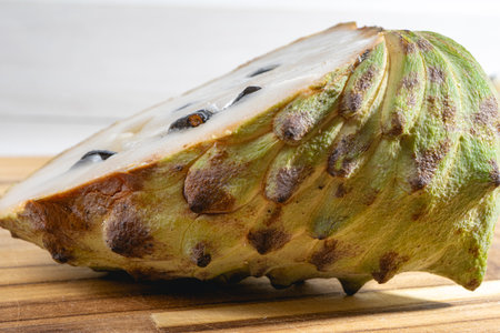 Atemoya, a tropical fuit, laying down on a wooden board, with a white background.