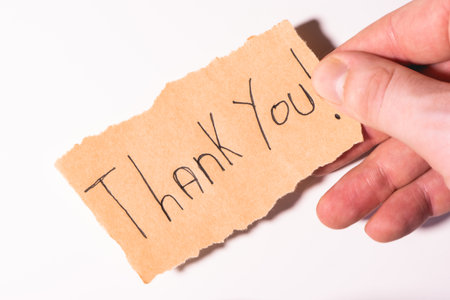 A handwriting Thank you note on brown paper, on a white background. With a hand and a pencil.の写真素材