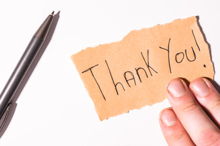 A handwriting Thank you note on brown paper, on a white background. With a hand and a pencil.の写真素材