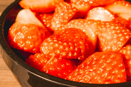 A black bowl of strawberry pieces, on a wooden background.の写真素材