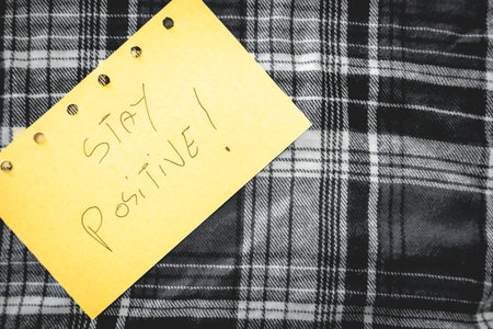 A handwritten note with Stay positive on it. Positive notes. on a white wooden  background.