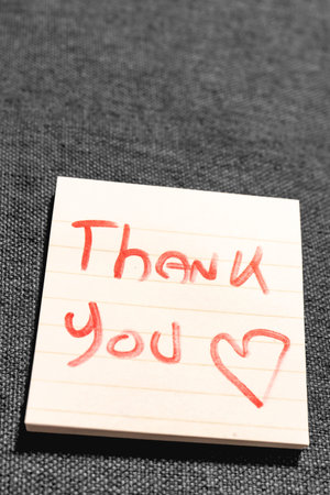 A handwritten note with the text Thank You  on it. On a grey background.