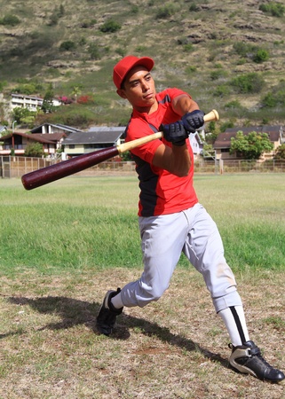 Baseball batter mid-swing in an open grassy fieldの写真素材