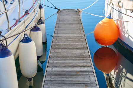 Marina with anchored boats - Perspective of small floating pier on still waterの写真素材