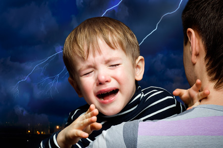 Crying boy in the hands of father on the background of lightningの写真素材