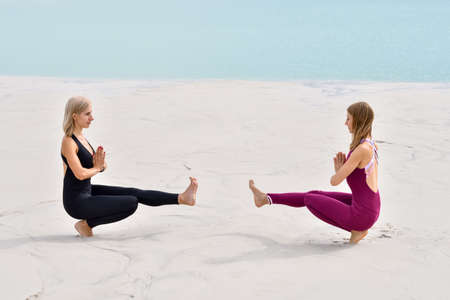 Two beautiful young women doing yoga on the beach