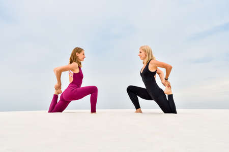 Two beautiful young women practice yoga on the sandの写真素材