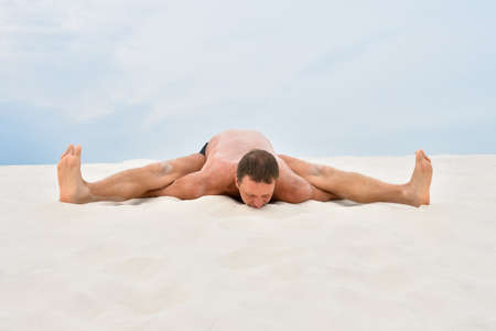 Young man in yoga pose kurmasana on the beachの写真素材