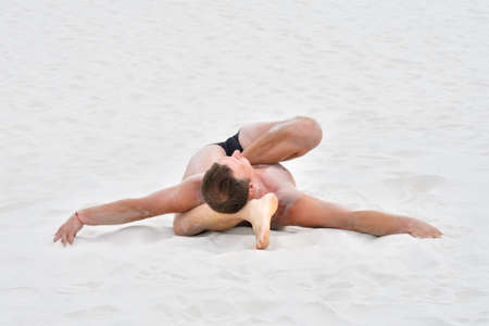 Young man in yoga pose on the sand at the beach