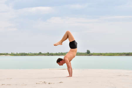 Man a yoga pose Vrishchikasana on the beach