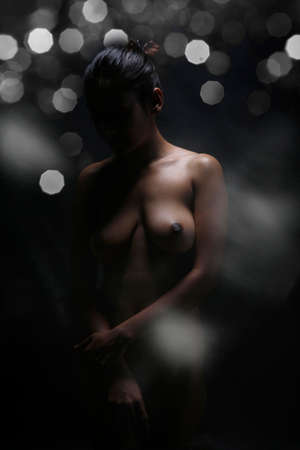 beautiful young nude woman from behind standing over black background and posing colorの写真素材