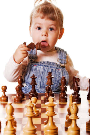  girl behind chess desk holding a chess piece in her hand and trying to taste it. Isolated on white background.の写真素材