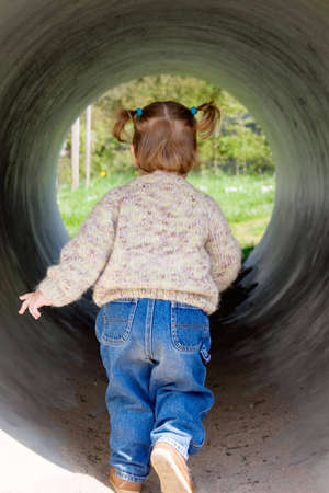 Little girl running away through the big tube on a playground.の写真素材