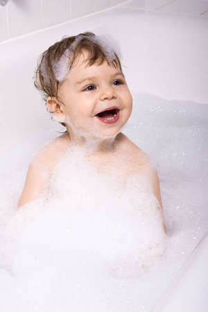 Laughing baby girl sitting in the bath full of shampoo foam.の写真素材