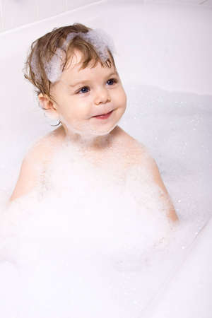 Baby girl sitting in the bath full of shampoo foam.の写真素材
