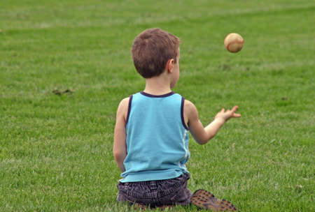 A young boy sitting in grass tossing baseballの写真素材