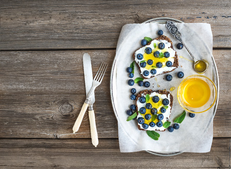 Healthy breakfast set with ricotta, fresh blueberries and honey sandwiches on whole grain bread served with mint on a silver dish over a rustic wood background with a copy space. Top viewの写真素材