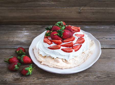 Rustic Pavlova cake with fresh strawberries and whipped cream over a rough wood backgroundの写真素材