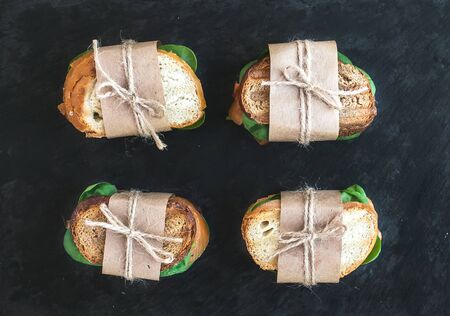 Chicken and spinach sandwiches wrapped in craft paper over a dark stone background. Top viewの写真素材