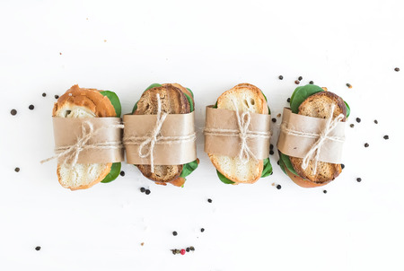 Chicken and spinach sandwiches wrapped in craft paper over a white wooden background with a copy...
