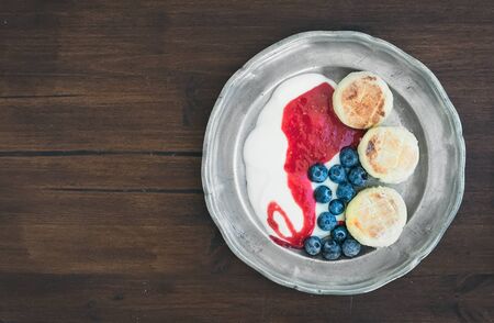 Breakfast set: curd pancakes with yogurt, fresh blueberry and raspberry jam on a vintage metal plate  over a dark wood background with a copy space. Top viewの写真素材