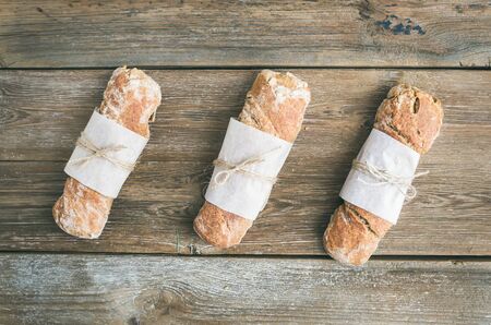 Freshly baked rustic  village bread (baguette) set on rough wood background. Top view