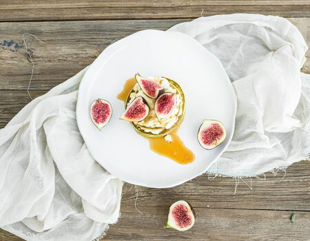 Marrow pancakes with fresh figs, honey and goat cheese on a white ceramic plate over linen fabric and rustic wood backgroundの写真素材