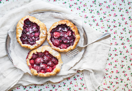 Small rustic berry galettes on silver dish over a floral patterned table clothの写真素材