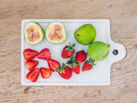 A set of fresh fruit on a white ceramic cutting board with a wooden backgroundの写真素材
