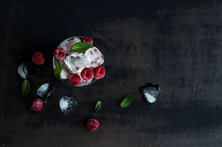 Ice cubes with mint leaves and frozen raspberry in glass on grunge dark background with copy spaceの写真素材