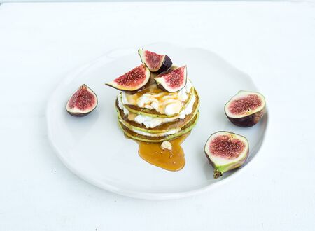 Marrow pancakes with fresh figs, honey and goat cheese on a white ceramic plate over a white backgroundの写真素材