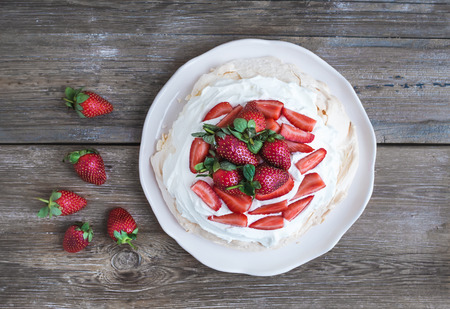 Rustic Pavlova cake with fresh strawberries and whipped cream over a rough wood background. Top viewの写真素材