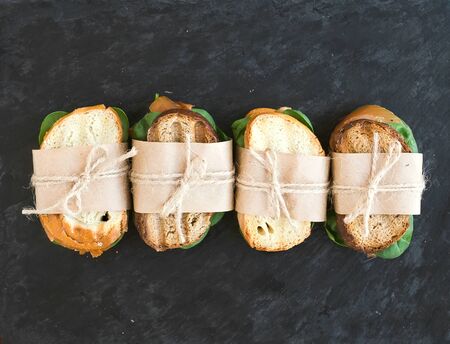 Chicken and spinach sandwiches wrapped in craft paper over a dark stone background with a copy spaceの写真素材