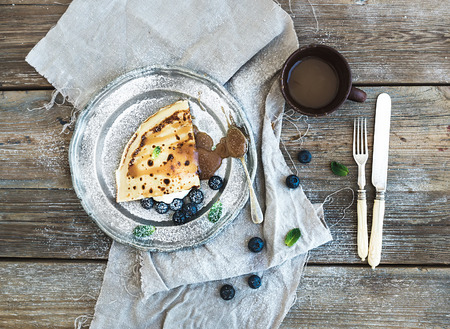 Thin pancake or crepe with fresh blueberry, cream, mint, and salty caramel sauce in vintage metal plate over rustic wooden backdrop. Top viewの写真素材