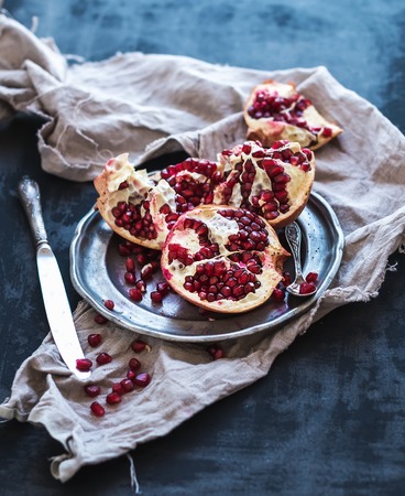 Red ripe peeled pomegranate on rustic metal plate and beige kitchen towel over dark background. Top view, copy spaceの写真素材