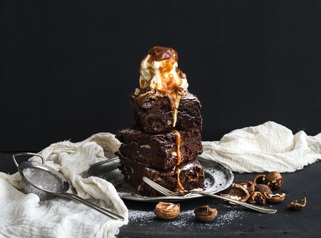 Fudgy Brownies tower with salted caramel, walnuts and ice-cream on vintage metal plate. Dark backdropの写真素材