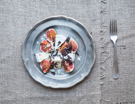 Dessert consisting of fresh figs and brie cheese with honey, almond petals and chocolate chips on a metal plate over a sackcloth backgroundの写真素材